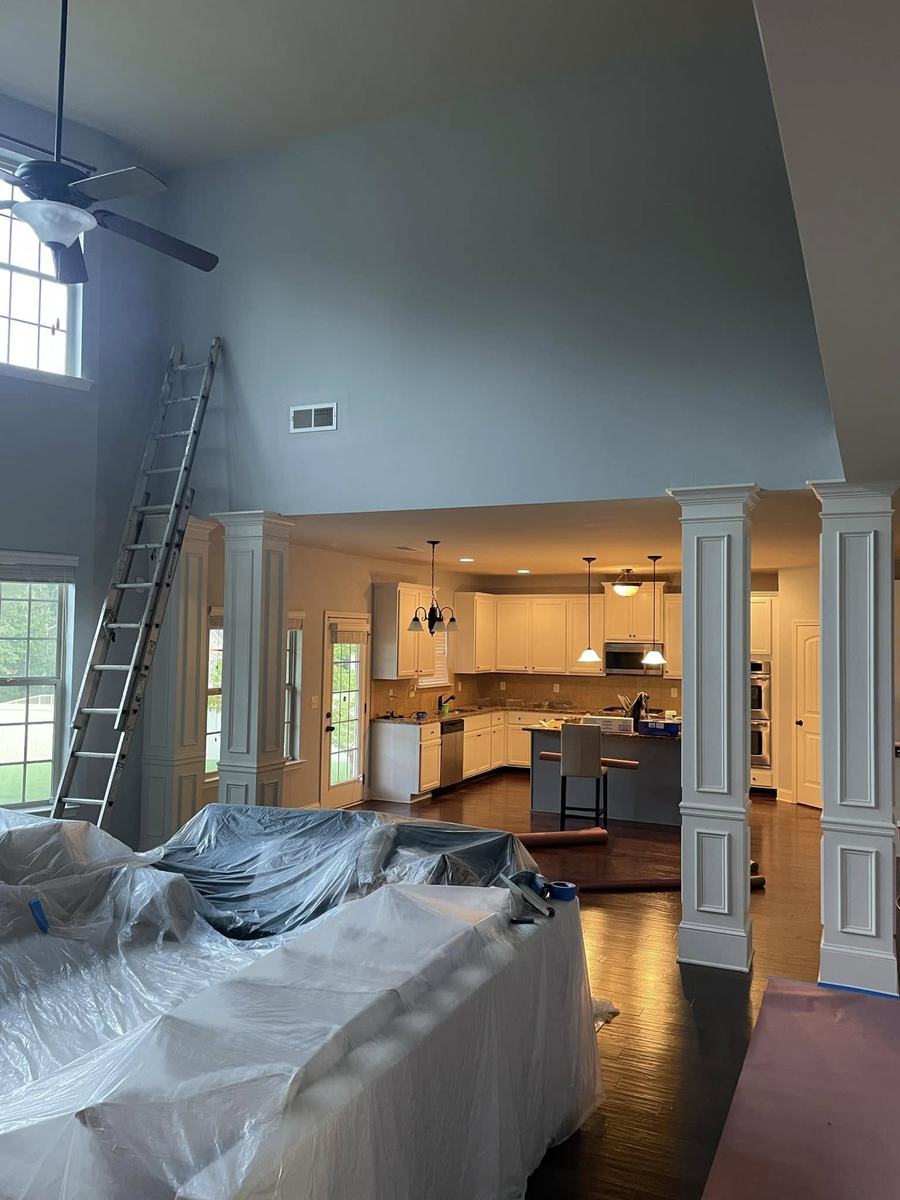 Great-room interior repaint in progress — furniture covered and protected, ladder set for the high walls